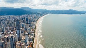 Vista aérea de uma cidade litorânea com uma alta densidade de arranha-céus margeando uma longa praia