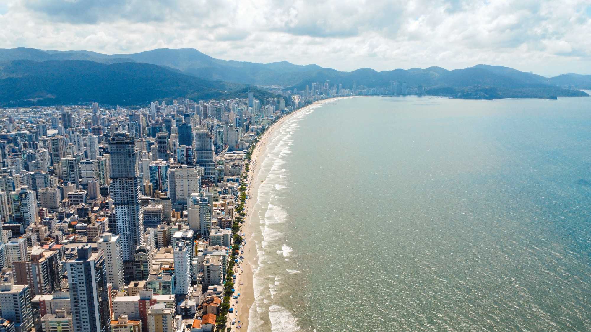 Vista aérea de uma cidade litorânea com uma alta densidade de arranha-céus margeando uma longa praia